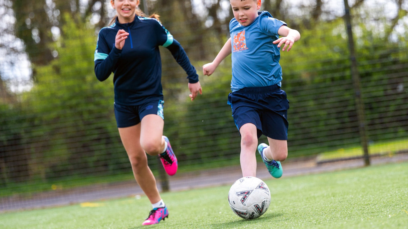 Image of a girl and boy playing football wearing football training clothing