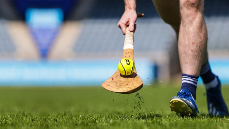 A player with hurley and sliotar on a pitch