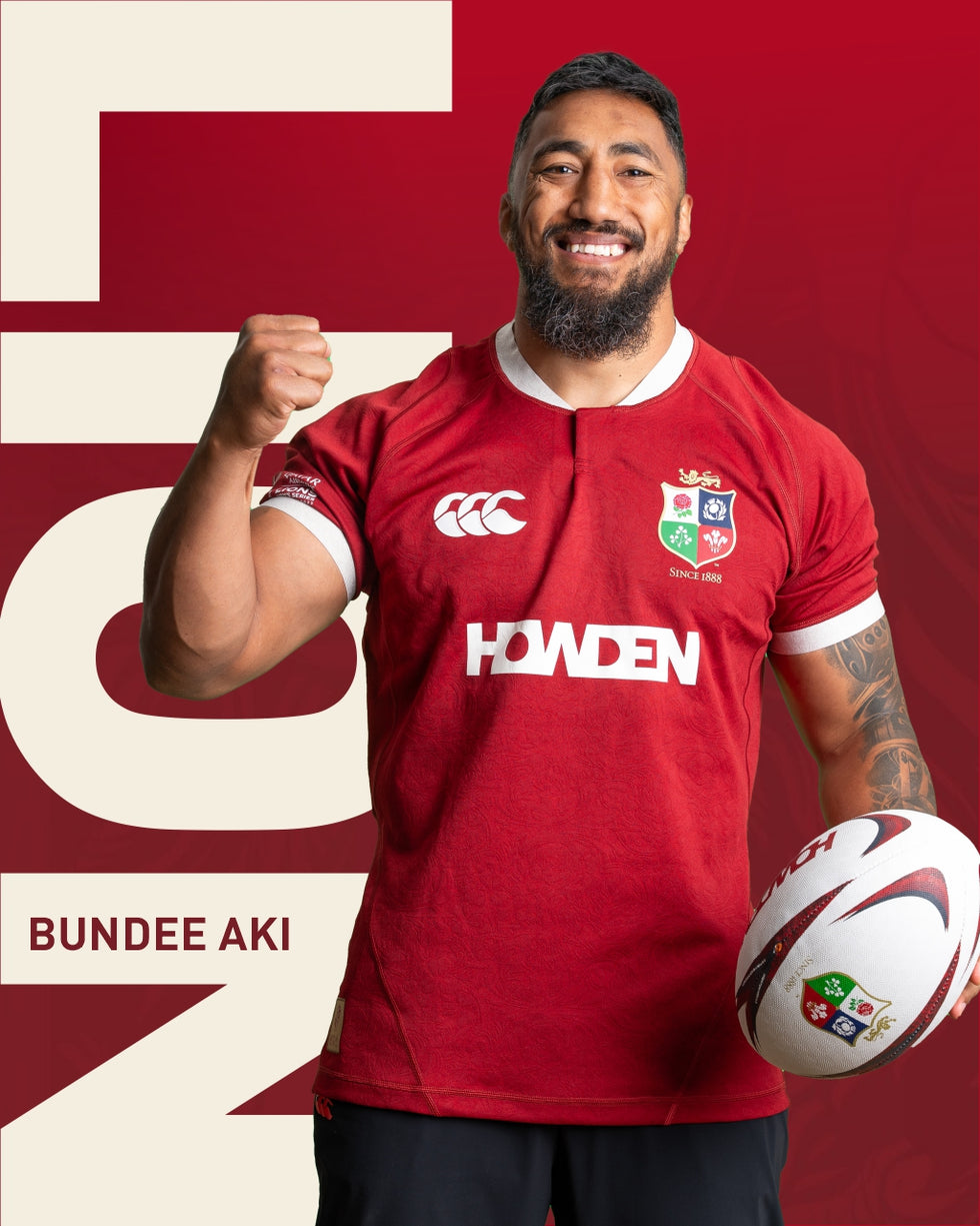 An image of Bundee Aki holding his arm in the air, holding the Lions rugby ball whilst wearing the 2025 British Irish Lions Jersey