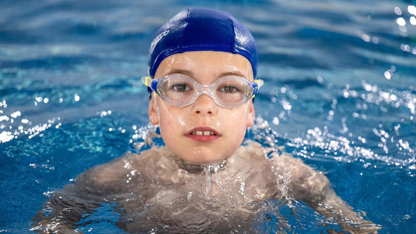 A boy with googles on in a swimming pool