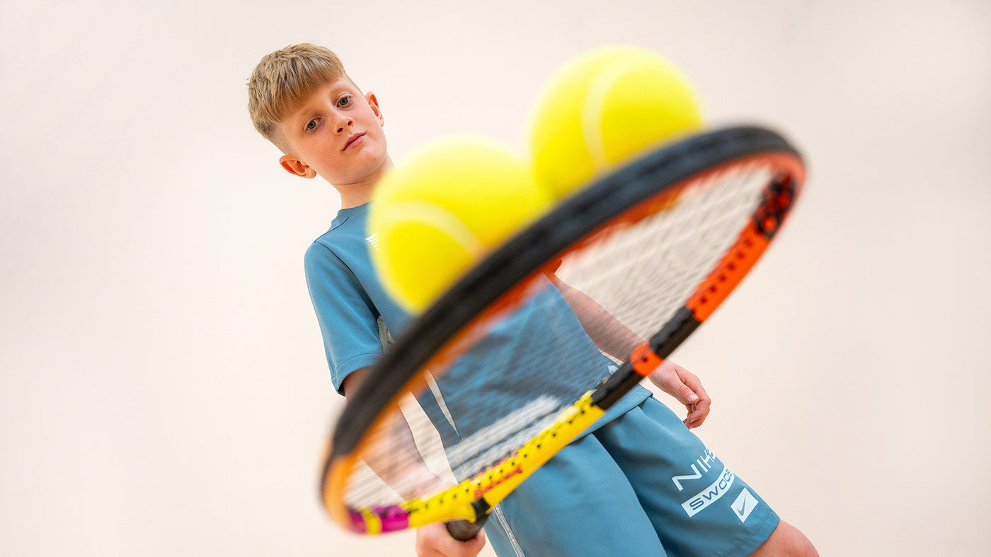 A boy playing with a tennis racket and tennis balls